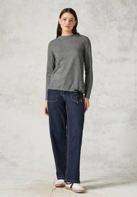 Grå långärmad topp med rundad halsringning och frontknutdetaljer, i kombination med löst sittande mörkblå jeans och vita sneakers.