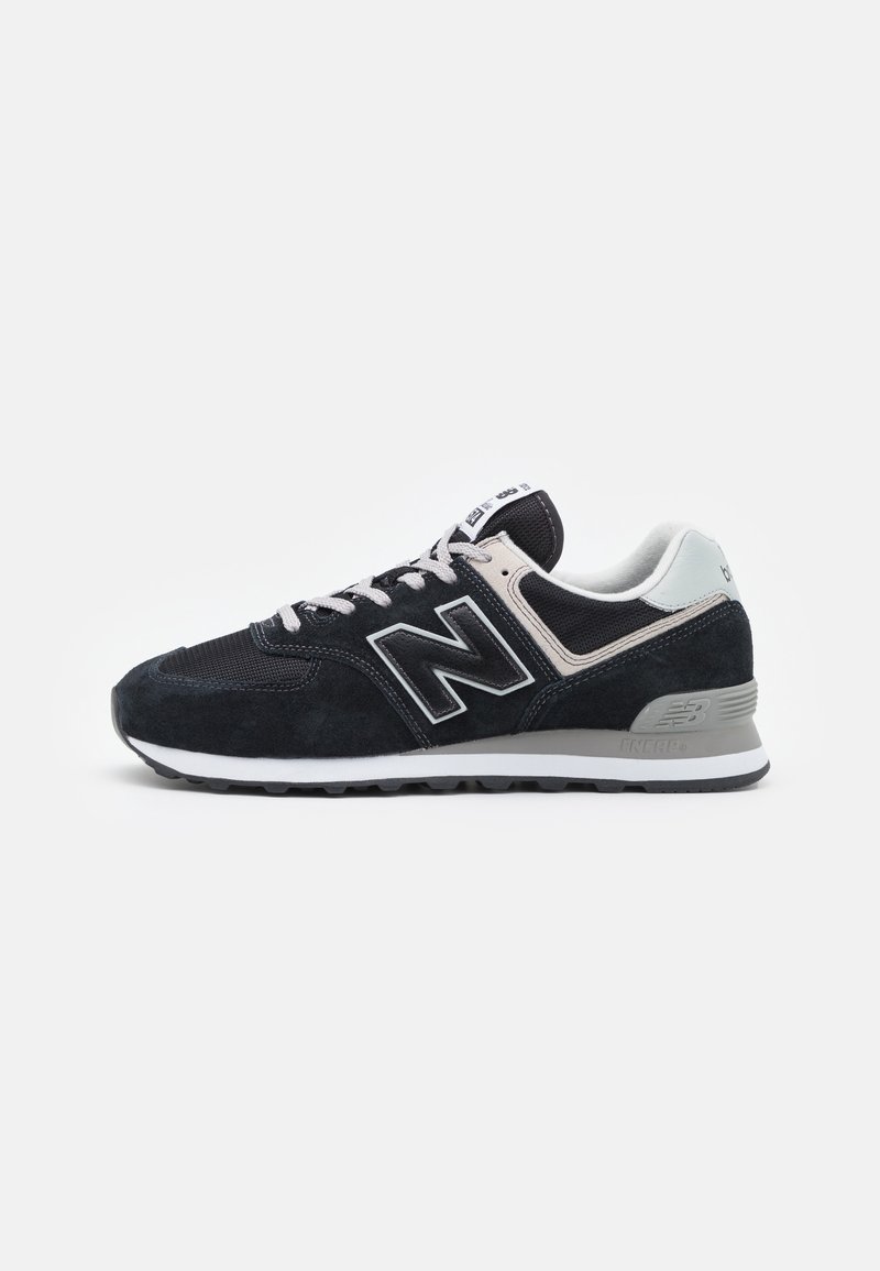 Sneaker atletica New Balance nero e grigio con suola bianca, lacci bianchi e parte superiore in rete e camoscio vista di lato su sfondo bianco.