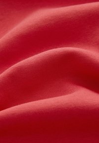 Gros plan d'un tissu rouge doux et lisse avec de légers plis et une texture tricotée visible, indiquant un matériau textile.