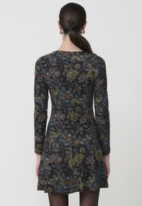 Vestido negro ajustado con mangas largas, que presenta coloridos patrones florales y de paisley, tejido texturizado y una falda acampanada.