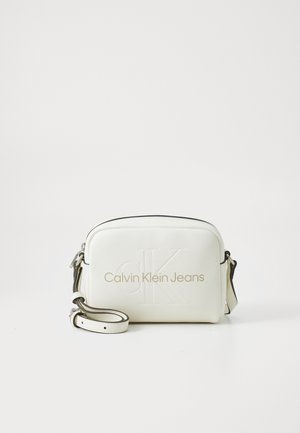 Hvid Calvin Klein Jeans crossbody taske med præget logo og justerbar rem på en ensfarvet hvid baggrund.