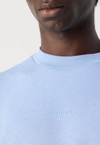 Sudadera de cuello redondo azul claro, hecha de una tela suave, con un cuello acanalado y un discreto logo "BOSS" en relieve en el pecho.