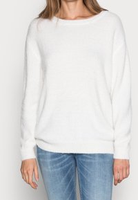 Maglione bianco, morbido, con una vestibilità rilassata, scollatura ampia e maniche lunghe. Tessuto a maglia con polsini e orlo a costine, abbinato a jeans blu.