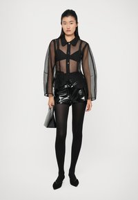 Čierna priesvitná blúzka s dlhými rukávmi a gombíkmi, vrstvená overa priliehavého čierneho tielka. Doplněné s čiernymi lesklými šortkami s vysokým pásom a čiernymi pančuchami.