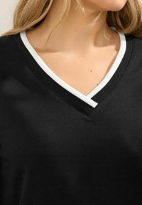 Suéter negro con cuello en V de tela texturizada, con un ribete blanco acanalado que contrasta a lo largo del escote. Diseño simple y funcional.
