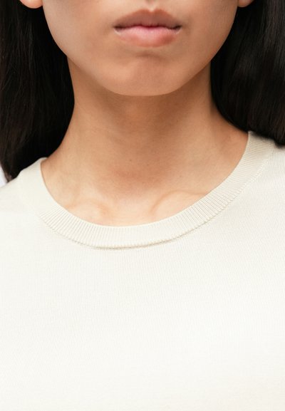 T-shirt en coton beige clair à côtes, avec un col arrondi et des détails de couture subtils, présentant une texture lisse.