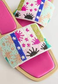 Sandales plates avec semelles roses et larges brides en tissu décorées de motifs colorés en perles en forme de soleil, d'étoile et de fleurs.