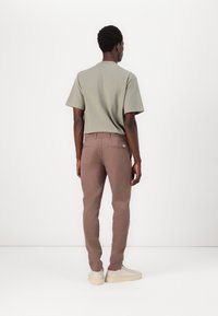 Camiseta de manga corta gris claro combinada con pantalones marrón ajustados y zapatillas beige. Dos bolsillos traseros en los pantalones con cremalleras.