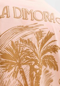 Gros plan sur un tissu rose avec une illustration de palmier marron et un texte partiel « LA DIMORA » en police stylisée.