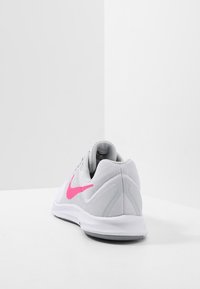 Scarpa sportiva bianca con accenti rosa, tomaia in rete, tallone rinforzato e suola in gomma testurizzata. Logo swoosh ben visibile sul lato.