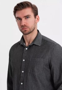 Chemise boutonnée gris foncé en tissu texturé, dotée d'une poche poitrine et de boutons blancs, avec un design de col classique.