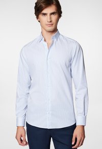 Koszula z długim rękawem w jasnoniebieskim kolorze z wąskimi pionowymi paskami. Posiada szpiczasty kołnierzyk oraz długie rękawy z guzikami przy mankietach. Gładka tekstura.