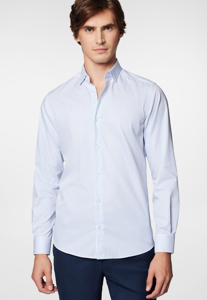 Koszula z długim rękawem w jasnoniebieskim kolorze z wąskimi pionowymi paskami. Posiada szpiczasty kołnierzyk oraz długie rękawy z guzikami przy mankietach. Gładka tekstura.