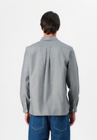 Camisa gris de manga larga con textura tejida y cuello desplegable, que cuenta con puños abotonados y un detalle de pliegue en la parte posterior.