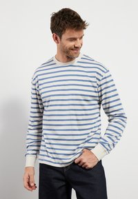 Langermet skjorte i kremfarge med blå horisontale striper. Har rund hals og mansjetter i kontrastfarge. Teksturert bomullsstoff.