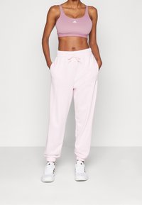 Ljusrosa sweatpants med elastiska mudd och dragsko i midjan, parat med en matchande rosa sport-bh med en vit logotyp.