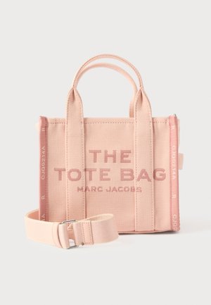 Sac fourre-tout en toile rose avec poignées courtes, bandoulière réglable, et texte en relief indiquant "THE TOTE BAG MARC JACOBS" sur le devant.