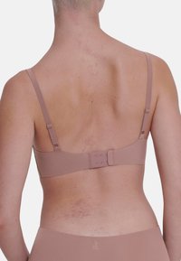 Lyserød bh med slanke stropper, hægte- og øjeknap bagpå og glat tekstur. Hudtone synlig med lette mærker.