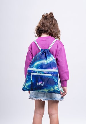Kind mit lockigem Haar, trägt ein pinkes Sweatshirt und einen Jeansrock, trägt einen blauen Kordelzug-Rucksack mit Nordlichtern und Baum-Design.