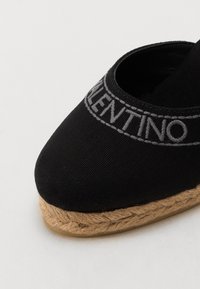 Juodas kanvoso espadrilės su apvaliu pirštu ir jūrinės virvės padu. Apatinėje dalyje išsiuvinėta pilka "Valentino" iškarpa.