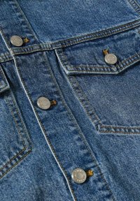 Chaqueta de mezclilla azul con botones metálicos plateados visibles y costuras amarillas en los bolsillos y las costuras.