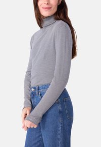 Schwarz-weiß gestreifter Rollkragenpullover mit langen Ärmeln, enganliegendes Design, weicher Stoff, kombiniert mit hochgeschnittenen blauen Jeans.