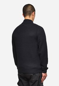 Dunkelblauer Strickpullover mit hohem Kragen, gerippten Bündchen und strukturiertem Muster. Entworfen mit einem lockeren Schnitt und sichtbaren Nähdetails.