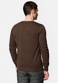 Brązowy sweter robiony na drutach z długimi rękawami i okrągłym dekoltem, z podwiniętymi mankietami i dolnym brzegiem. Gładka tekstura, minimalistyczny design.