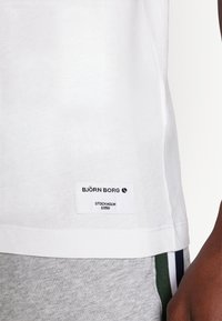 White cotton T-shirt with a stitched tag reading "BJÖRN BORG," featuring subtle texture and a round neckline, paired with gray bottoms.