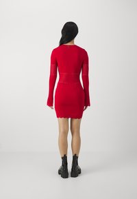 Abito bodycon rosso a maniche lunghe con dettagli in rete a taglio, orlo scallop e motivo sulle maniche. Abbinato a stivaletti neri alla caviglia.