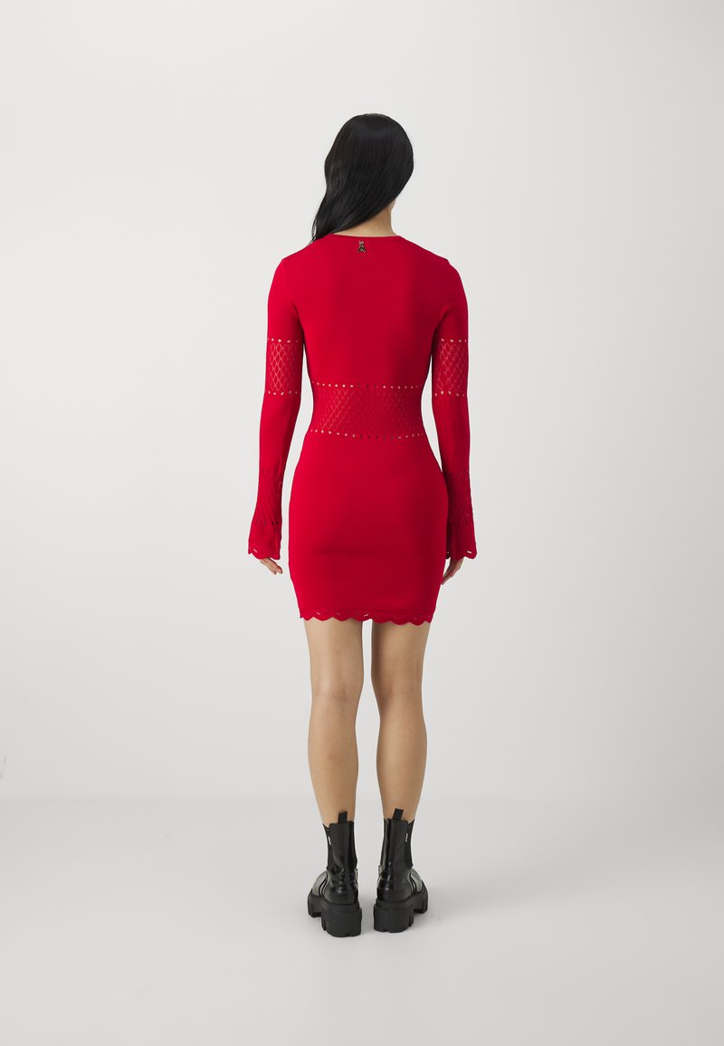 Abito bodycon rosso a maniche lunghe con dettagli in rete a taglio, orlo scallop e motivo sulle maniche. Abbinato a stivaletti neri alla caviglia.