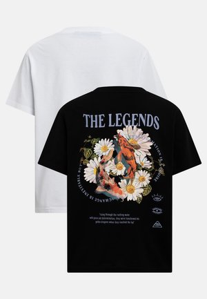Zwart T-shirt met madeliefjes, koi-karpers en de tekst "THE LEGENDS," gedragen over een eenvoudig wit T-shirt.