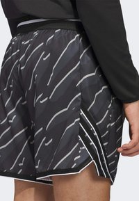 Mustat urheilushortsit, joissa on harmaa abstrakti kuvio, verkko-sivupaneeli valkoisilla raidoilla ja musta vyötärö.