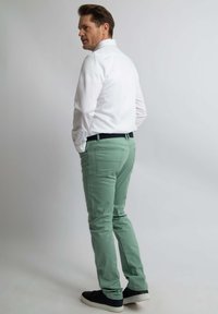 Weißes Langarmhemd, mintgrüne Slim-Fit-Hose und dunkle Sneakers. Sichtbare Gesäßtaschen und ein Gürtel mit dunkler Schnalle. Minimalistisches Design.