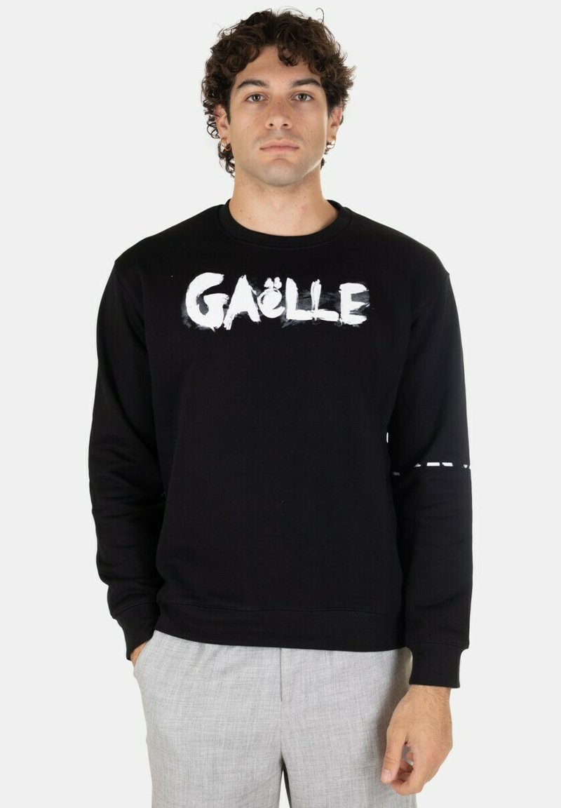 Felpa nera con testo bianco "GÄLLE" sul petto, in materiale di cotone, maniche lunghe e un dettaglio cucito sul braccio sinistro.