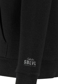Black sweatshirt featuring a ribbed hem and cuffs. Textured fabric with a logo print on the sleeve reading "Collection SBLVL Urban Edition."