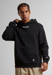 Schwarzer Hoodie aus weichem Baumwollmaterial mit einer Vordertasche, der ein weißes "Starter"-Logo auf der Brust und ein kleines Emblem am Ärmel hat.