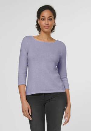 Pull long violet à manches longues avec un col rond, texture douce et coupe ajustée, associé à un jean foncé. Fini au tissu lisse.