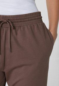 Braune Baumwoll-Jogginghosen mit elastischem Bund und Kordelzug. Mit Seitentaschen und einer weichen Textur. Nahaufnahme des Stoffs.