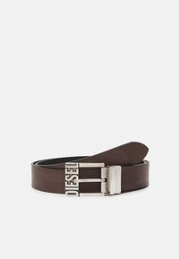Ceinture en cuir marron avec une boucle en métal argenté portant le nom de la marque gravé. Texture lisse et extrémité arrondie pour le fixation.