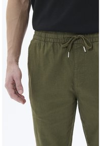 Olive green, lightweight pants with an elastic waistband and adjustable drawstring. Features side pockets and smooth texture.