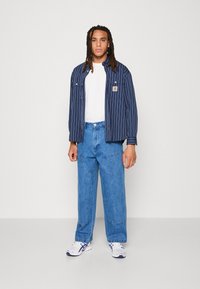 Navy striped jacket over a white t-shirt, paired with loose blue jeans and white sneakers with blue accents. Casual outfit with distinct textures.