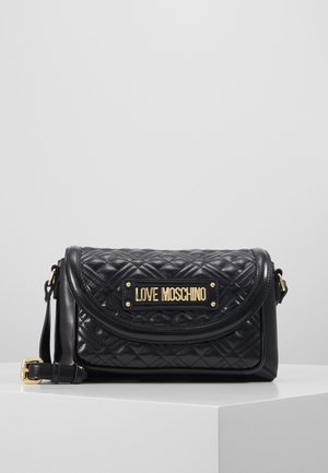 Sac à bandoulière en cuir matelassé noir avec plaque logo dorée "LOVE MOSCHINO" et bandoulière réglable sur une surface d'affichage blanche.