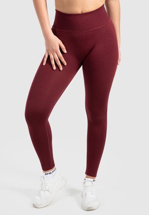 Bordeaux hoge taille legging gemaakt van rekbare stof. Zachte textuur met een strakke pasvorm, gecombineerd met witte sportschoenen.