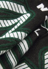 Tecido com uma base preta e padrões de folhas verdes e brancas, exibindo uma superfície texturizada e detalhes de listras contrastantes.