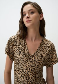 Beige v-hals top met luipaardprint en korte mouwen, voorzien van zwarte vlekken en een zachte, gladde textuur. Eenvoudig, casual ontwerp.