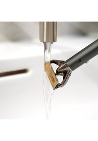 Metallbarberhøvel med blad i gullfarge, vann strømmer over det fra en rustfri stålkran, hviler over en hvit vask.