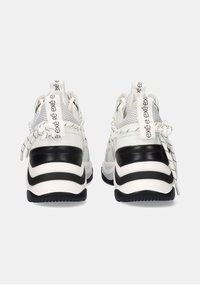 Zapatillas deportivas blancas con suelas a rayas en negro y blanco, detalles de malla y una marca prominente en el talón. Los cordones están atados en la parte trasera.