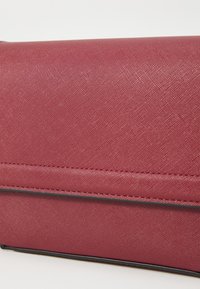 Teksturert mørkerødt håndveske med glatt overflate, med sort kant og subtile sømdetaljer langs kanten.