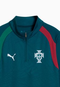 Tummanvihreä urheilupaita, jossa on puolivetoketju, vihreät ja punaiset olkapääpaneelit, valkoinen Puman logo vasemmalla ja Portugalin jalkapallojoukkueen vaakuna oikeassa rinnassa.